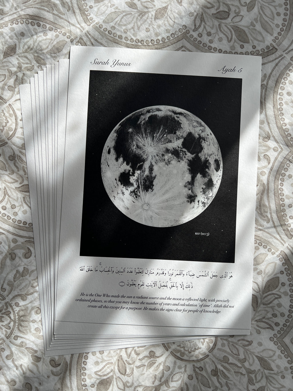 Stack of minimalistic islamic prints depicting the verse (10:5) with a monochrome full moon on a black background. Below is the verse it is inspired by. The perfect reminder and decor for any muslim.